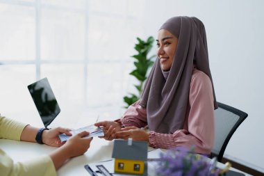 Müslüman bir kadın banka çalışanı, bir müşteriyle konut kredisi anlaşması yapıyor.