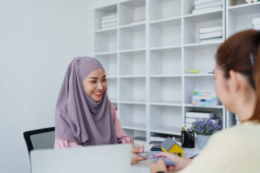 Müslüman bir kadın banka çalışanı, bir müşteriyle konut kredisi anlaşması yapıyor.