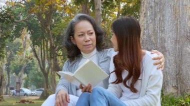 Bir büyükanne ve en büyük torunu bir ağacın altında kitap okurken oturup sohbet ediyorlar. Yüksek kalite 4k görüntü