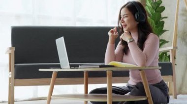 Evde bilgisayar, dizüstü bilgisayar ve dizüstü bilgisayar kullanarak kulaklık takan Asyalı çekici genç kız öğrenci. Yüksek kalite 4k görüntü