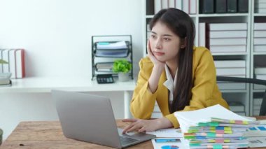 Genç Asyalı bir iş kadını büroda bilgisayar ve evrak işleriyle uğraşmaktan bıkkınlık ve yorgunluk gösteriyor, tükenme sendromu, yorgun ve endişeli kavramlar. Yüksek kalite 4k görüntü