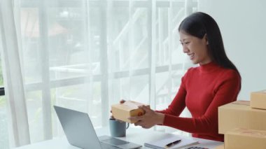 Küçük işletme, sme, Asyalı güzel kadın müşterilerle video konferans kullanarak ürün kutusunun boyutunu görüyor ve müşteriye verilecek fiyatı söylüyor.