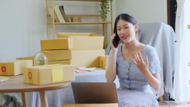 Bağımsız Asyalı kadın çevrimiçi satıcının küçük işletme girişimcisi olarak bir müşteriyle telefonda konuşuyor ve müşteriye teslimat için ürünleri paketliyor. ve KOBİ teslimat konsepti. Yüksek