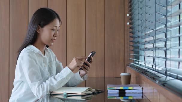 Молодая Азиатка Пользующаяся Мобильным Смартфоном Делает Заметки Блокноте Счастливым Выражением — стоковое видео
