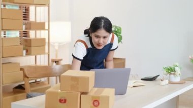 Küçük bir girişimin portresi ve KME sahibi, Asyalı bir bayan girişimci not defterleri ve dizüstü bilgisayar kullanarak müşteriler için iç kutulara koymadan önce ürünleri organize etme talimatlarını kontrol ediyor. Yüksek