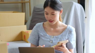 Bağımsız genç Asyalı kadın çevrimiçi satıcının küçük işletme girişimciliğine başlamak, bilgisayar kullanmak ve müşterilere dağıtım için ürünleri paketlemek için siparişler almaktır. KOBİ teslimat konsepti. 4k görüntü
