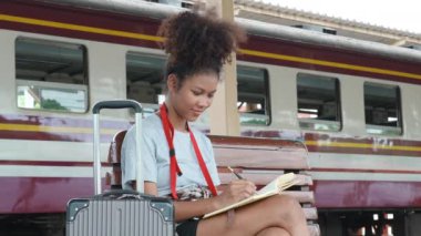 Afro-Amerikan turistler tren istasyonunda yolculuklarını beklerken hatıra defterlerini kullanıyorlar. Yüksek kalite 4k görüntü