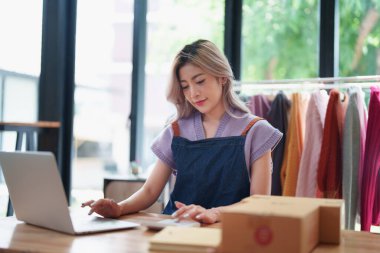 Bağımsız genç Asyalı kadın çevrimiçi satıcının küçük işletme girişimciliğine başlamak, bilgisayar kullanmak ve müşterilere dağıtım için ürünleri paketlemek için siparişler almaktır. KME dağıtım kavramı.