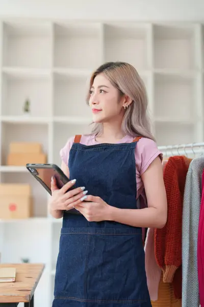 Portrait Of Asian Female Owner Of Fashion Store Checking Stock In Clothing Store With using notebook successful happy smile at small business, sme or ecommerce concepts.