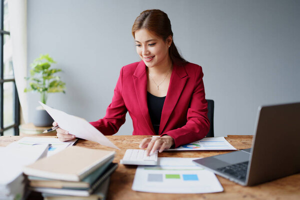 businesswoman or accountant working on calculator and laptop computer to calculate business data during using accountancy document at office.