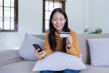 Kadın internet üzerinden alışveriş yapmak için kredi kartını kullanıyor, akıllı telefonundaki çeşitli mağazaları geziyor..