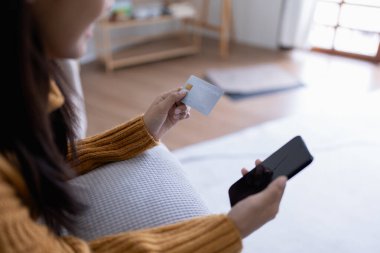 Kadın internet üzerinden alışveriş yapmak için kredi kartını kullanıyor, akıllı telefonundaki çeşitli mağazaları geziyor..