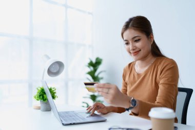 Kadın internet üzerinden alışveriş yapmak için kredi kartını kullanıyor. Bilgisayarındaki çeşitli mağazaları geziyor..