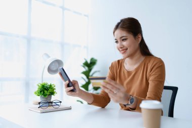 Kadın internet üzerinden alışveriş yapmak için kredi kartını kullanıyor, akıllı telefonundaki çeşitli mağazaları geziyor..