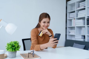 Kadın internet üzerinden alışveriş yapmak için kredi kartını kullanıyor, akıllı telefonundaki çeşitli mağazaları geziyor..