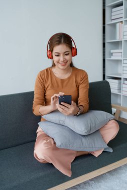 Bir kadın kulaklıklarıyla oturup akıllı telefonuyla müzik dinlerken kendini tamamen rahat hisseder..