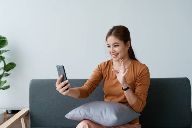 Kadın kanepede dinlenir, rahat hisseder ve akıllı telefonuyla video aramasından zevk alır..