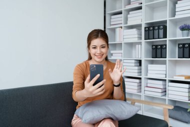 Kadın kanepede dinlenir, rahat hisseder ve akıllı telefonuyla video aramasından zevk alır..