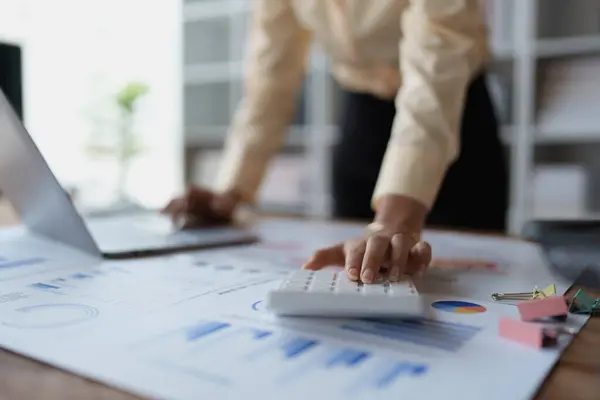 stock image woman meticulously plans a finance audit, using a computer and calculator to review budget documents and ensure accuracy.