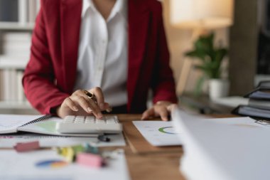Kadın, bütçe belgelerini gözden geçirmek ve doğruluğu sağlamak için bilgisayar ve hesap makinesi kullanarak titizlikle mali denetim planlıyor..