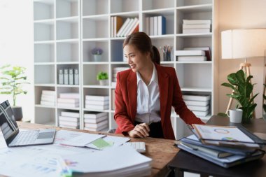 Kadın, bütçe belgelerini gözden geçirmek ve doğruluğu sağlamak için bilgisayar ve hesap makinesi kullanarak titizlikle mali denetim planlıyor..
