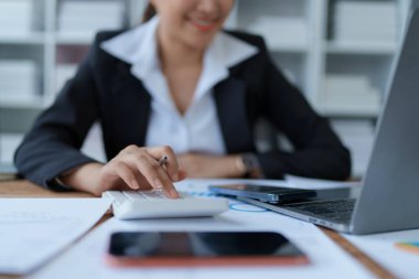 Kadın, bütçe belgelerini gözden geçirmek ve doğruluğu sağlamak için bilgisayar ve hesap makinesi kullanarak titizlikle mali denetim planlıyor..