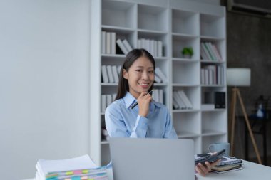 Kadın, bütçe belgelerini gözden geçirmek ve doğruluğu sağlamak için bilgisayar ve hesap makinesi kullanarak titizlikle mali denetim planlıyor..