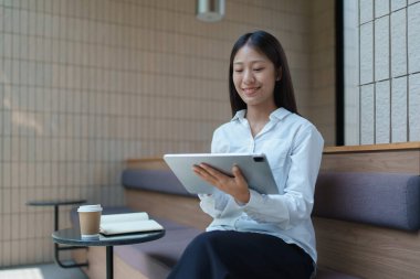 Modern kahve dükkanında tablet kullanan genç bir kadın, şık bir masada defter ve kahveyle..