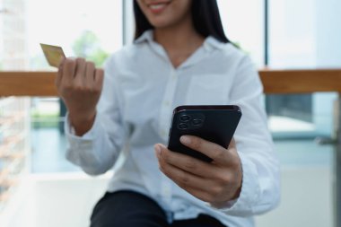 Modern kapalı alanda online alışveriş yaparken elinde akıllı telefon ve kredi kartı tutan genç bir kadın..