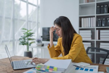 Modern bir ofis ortamında dizüstü bilgisayarla çalışırken strese giren iş kadını bunalmış..