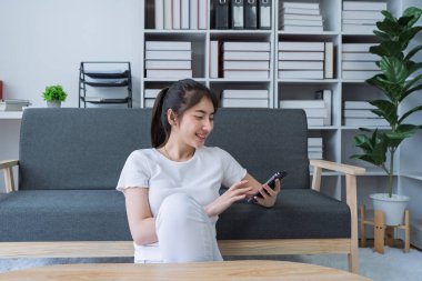 Kadın akıllı telefon kullanarak bir kanepede oturuyor ve evinde dinlenirken sosyal medyaya bağlanıyor..