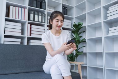 Kadın akıllı telefon kullanarak bir kanepede oturuyor ve evinde dinlenirken sosyal medyaya bağlanıyor..