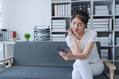Kadın akıllı telefon kullanarak bir kanepede oturuyor ve evinde dinlenirken sosyal medyaya bağlanıyor..