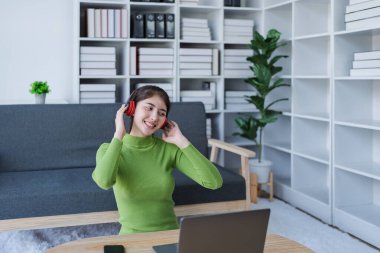 Kanepede dinlenen kadın kulaklık takıyor, rahat evde bilgisayar kullanırken müzik dinliyor..
