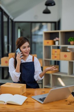 Genç bir kadın, modern ofis ortamında ürünleri dağıtırken çevrimiçi bir telefon görüşmesinde yer alıyor..