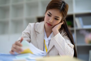 Stresli genç iş kadını mali işler, piyasa çizelgeleri ve bürodaki belgelerle boğulmuş durumda..