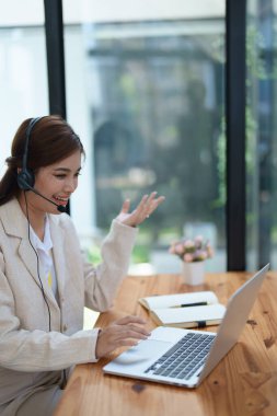 Asyalı iş kadını, çevrimiçi bir video konferansında pazarlama ve finans stratejilerini tartışırken kulaklık takıyor..