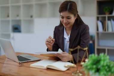 Bir hukuk firmasında kadın avukat. Masasında dizüstü bilgisayar ve adalet terazileriyle donatılmış yasal belgeleri inceliyor..