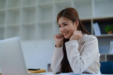 Kendine güvenen iş kadını gülümsüyor. Masasında başarılı jestler sergiliyor..