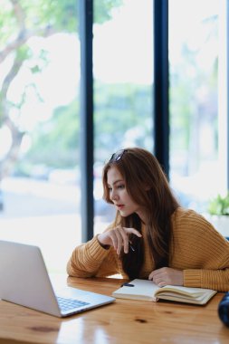 Gülümseyen genç bir kadın, neşeli bir e-öğrenme videosuyla meşgul. Kulaklıklı bir kitabı yakındaki tahta bir masada tutarken el kol hareketi yapıyor..
