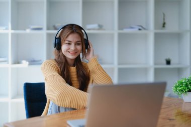 Genç bir kadın masasında dinlendirici bir müzik molası verirken kulaklık kullanıyor, deftere yazıyor ve sakin bir ilham için dizüstü bilgisayarı üzerinde çalışıyor..