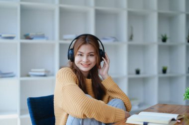 Genç bir kadın masasında dinlendirici bir müzik molası verirken kulaklık kullanıyor, deftere yazıyor ve sakin bir ilham için dizüstü bilgisayarı üzerinde çalışıyor..