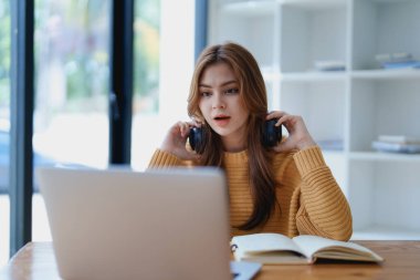 Genç bir kadın masasında dinlendirici bir müzik molası verirken kulaklık kullanıyor, deftere yazıyor ve sakin bir ilham için dizüstü bilgisayarı üzerinde çalışıyor..