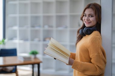 Kulaklıklı mutlu genç kadın bir kitaba dalmış, mutlu bir şekilde öğreniyor..