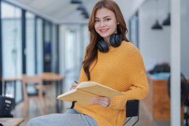 Kulaklıklı mutlu genç kadın bir kitaba dalmış, mutlu bir şekilde öğreniyor..