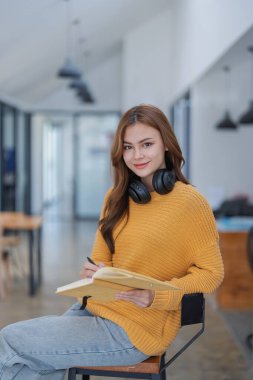 Kulaklıklı mutlu genç kadın bir kitaba dalmış, mutlu bir şekilde öğreniyor..