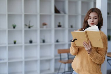 Kazaklı genç kadın, rahat evdeki modern kitaplığın yanında kitap okuyor...