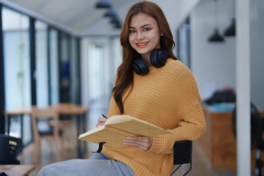 Gülümseyen genç bir kadın, kulaklık takarken deftere bir şeyler yazıyor...