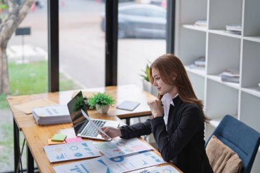 Genç iş kadını çalışma masasında çizelgeleri ve grafikleri dikkatlice analiz eder...