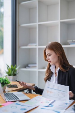 Odaklanmış iş kadını, ofisindeki bilgisayarında çizelgeleri ve grafikleri analiz eder...